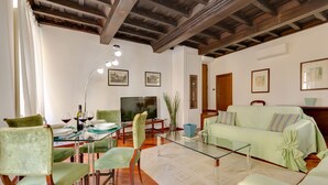 A dining area with a glass table, green upholstered chairs, and a wooden ceiling. - Panisperna Apartment | Comfortable and bright in Monti  (Roma)