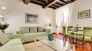 A living room with a green sofa, a glass coffee table, and a dining area with green chairs and a glass table. - Panisperna Apartment | Comfortable and bright in Monti  (Roma)