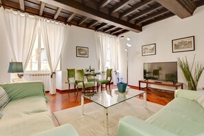 Ein Wohnzimmer mit einem Glastisch, grünen Sofas, einem Fernseher und gerahmten Bildern an der Wand.