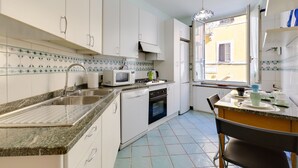 A compact kitchen with white cabinets, a granite countertop, a microwave, a stove, and a sink. - Panisperna Apartment | Comfortable and bright in Monti  (Roma)