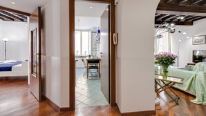 A modern interior with a wooden floor, a dining area with a table and chairs, and a kitchen in the background. - Panisperna Apartment | Comfortable and bright in Monti  (Roma)