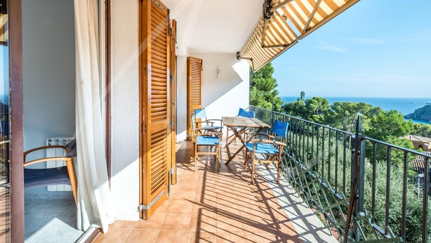 Un balcon avec une table et des chaises en bois, une vue sur la mer et une balustrade.