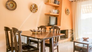 Un coin repas avec une table et des chaises en bois, un téléviseur et des assiettes décoratives accrochées au mur.