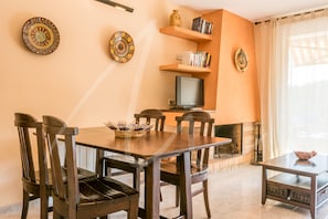 A dining area with a wooden table and chairs, a television, and decorative plates on the wall.