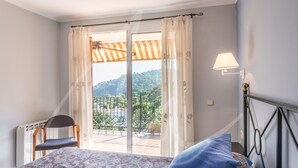 Une chambre à coucher comprenant un lit, une chaise, une fenêtre avec des rideaux et une vue sur un balcon doté d’une balustrade.