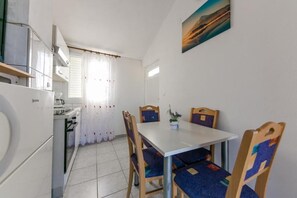 A compact kitchen with a dining area, featuring a table and chairs, a window with curtains, and a painting on the wall.