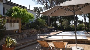 Un espace piscine extérieur agrémenté d’un mur en pierre, d’un grand arbre et d’une pergola avec un parasol.