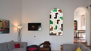 Un salon avec deux canapés gris, une table basse en bois, un tapis rouge et noir, un téléviseur et une fenêtre à vitraux.