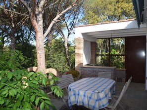 Eine Terrasse im Freien mit Tisch und Stühlen, umgeben von Grünpflanzen und einem großen Baum.