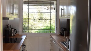 Une cuisine moderne avec des meubles blancs, des appareils en acier inoxydable et une fenêtre ornée d’une grille métallique.