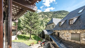 A stone building with a sloped roof, a wooden balcony, and a stone pathway leading to a grassy area with flowers.