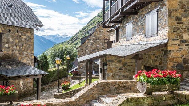 A stone building with a balcony, a stone staircase, and flower planters.