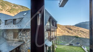 A view from inside a building looking out at a stone house with a balcony, surrounded by hills.
