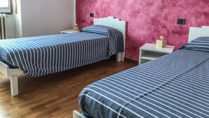 Une chambre avec deux lits, chacun doté de draps à rayures, d’un mur rose à texture et d’une tête de lit blanche.
