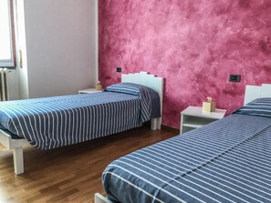 A room with two beds, each with striped bedding, a pink textured wall, and a white headboard.