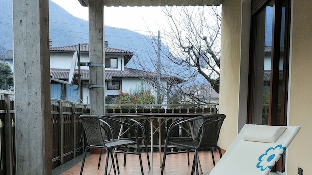 Un espace extérieur abrité comprenant deux chaises longues, une table avec des chaises, et une vue sur des bâtiments et des montagnes en arrière-plan.