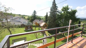 A balcony with a metal railing overlooking a residential area with houses, a wooden play structure, and a grassy yard. - Haus Buchholz Apartment 3   (Liesenich)