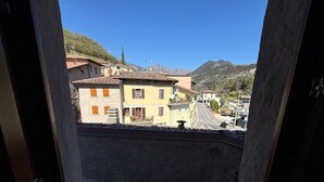 A view through a window of a building with a street, houses, and mountains in the background. - La Rotonda Vigneto Apartment (Tremosine)