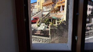 A view through a window of a building with multiple floors, balconies, and a red car parked outside. - La Rotonda Vigneto Apartment (Tremosine)