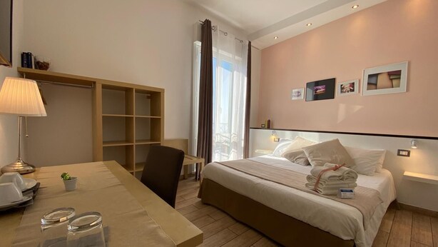 Una habitación de hotel con cama, mesita de noche, lámpara, silla y vistas a la ciudad a través de la ventana.