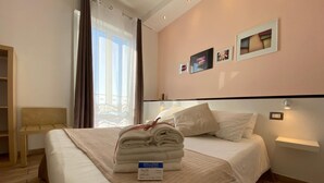 Habitación de hotel con cama, mesita de noche, estante en la pared y ventana con cortinas.