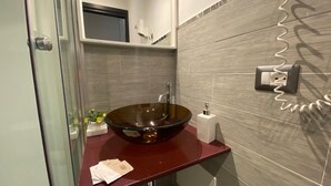 Un baño moderno con un lavabo de fondo de cristal, una encimera roja y un espejo encima.