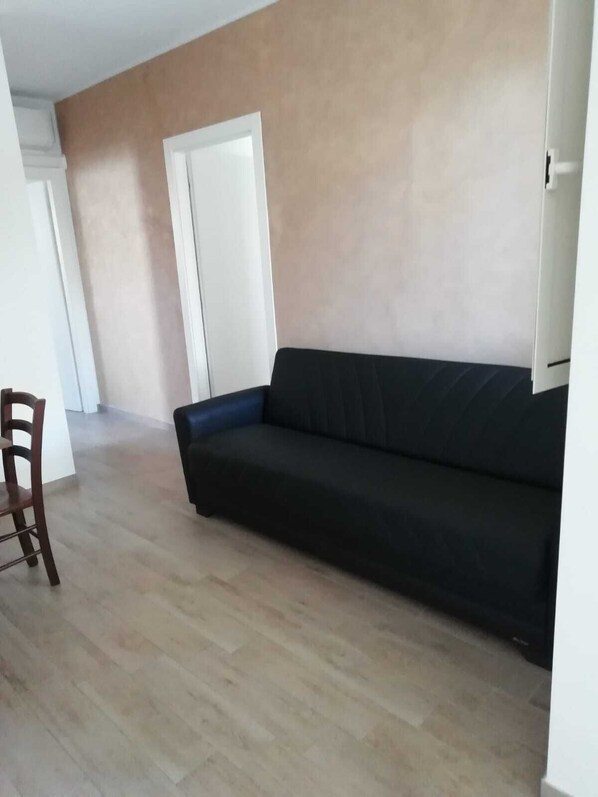 Een woonkamer met een zwarte bank, een houten stoel en een witte deur.