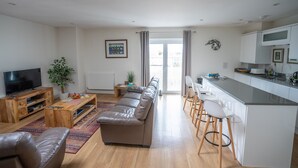 A modern living room with a sofa, TV, wooden coffee table, and a dining area with bar stools. - Very popular modern 2 bedroom apartment sleeps 4  located opposite Deal Pier.   (Deal)