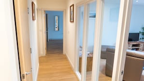 A hallway with wooden flooring, a sliding glass door leading to a living area with a sofa and a TV stand. - Very popular modern 2 bedroom apartment sleeps 4  located opposite Deal Pier.   (Deal)