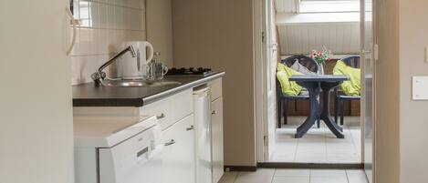 Een moderne keuken met witte kastjes, een ingebouwde vaatwasser en een eethoek met een tafel en stoelen.