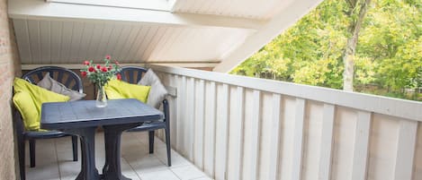 Un balcón con mesa y sillas, una planta en maceta y vistas a árboles.