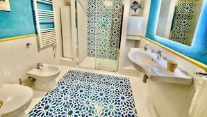 Een badkamer met een douche, twee wastafels, een toilet en een decoratieve spiegel.