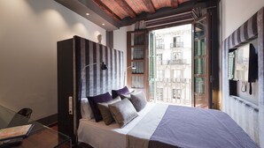 A modern bedroom with a bed, a desk, and a view of a building through a window.