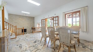 Um quarto amplo com lareira de pedra, área de jantar com cadeiras de vime e janelas grandes com cortinas.