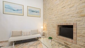 Uma sala de estar moderna com parede de pedra, lareira, mesa de centro de vidro e sofá branco.