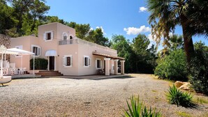 Uma casa de dois andares com entrada de automóveis em cascalho, área de estar ao ar livre e varanda coberta.