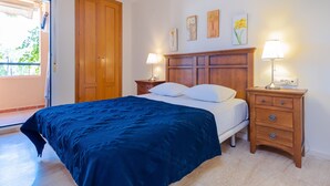 A bedroom with a bed, two bedside tables with lamps, a wooden wardrobe, and artwork on the wall. - Apartment only 80 Meters from the Beach (Marbella)