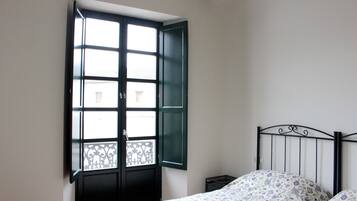 Une chambre avec un lit, une fenêtre dont les volets sont ouverts et une petite table de chevet.