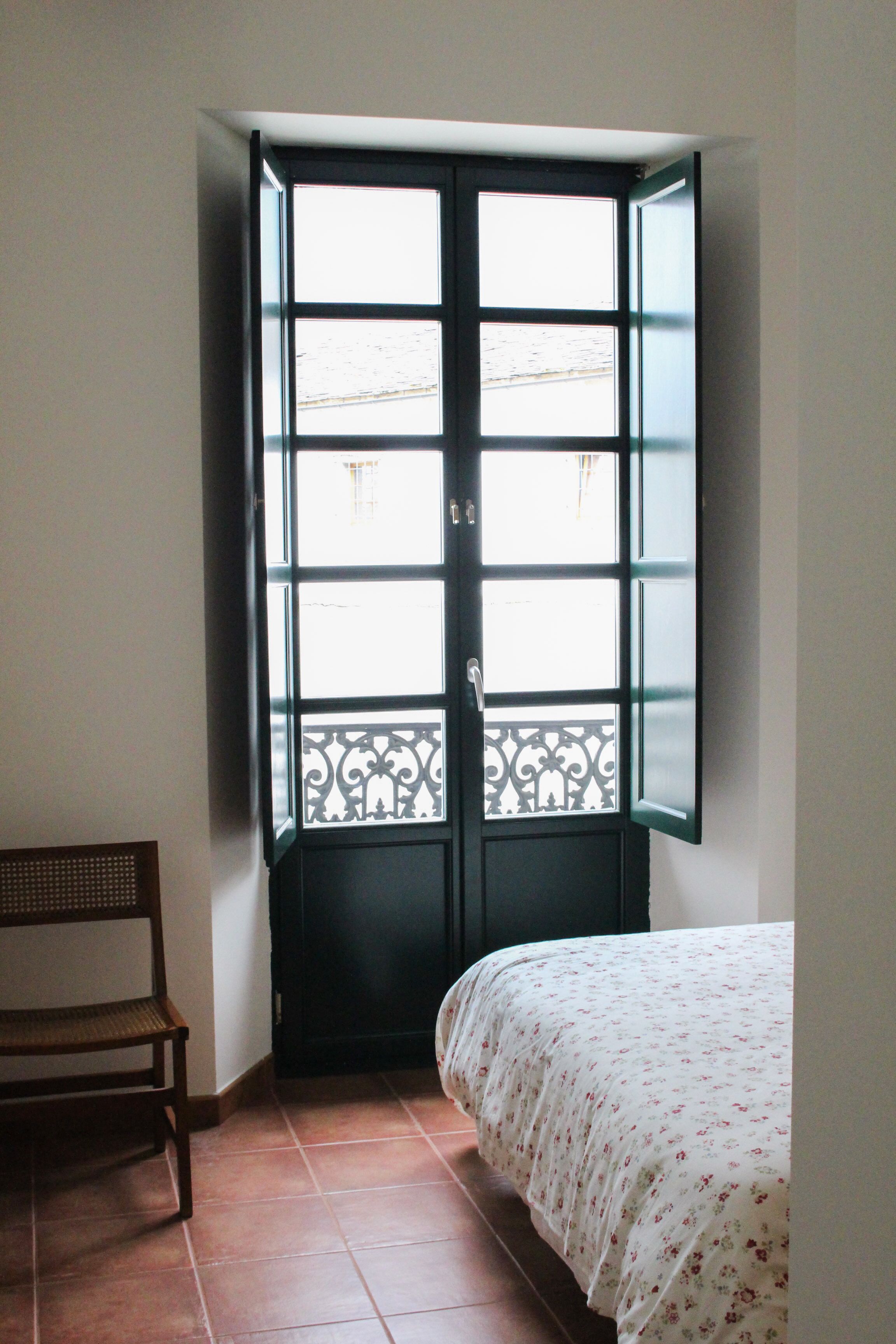 Quarto com cama, cadeira e janela com vista para o exterior.