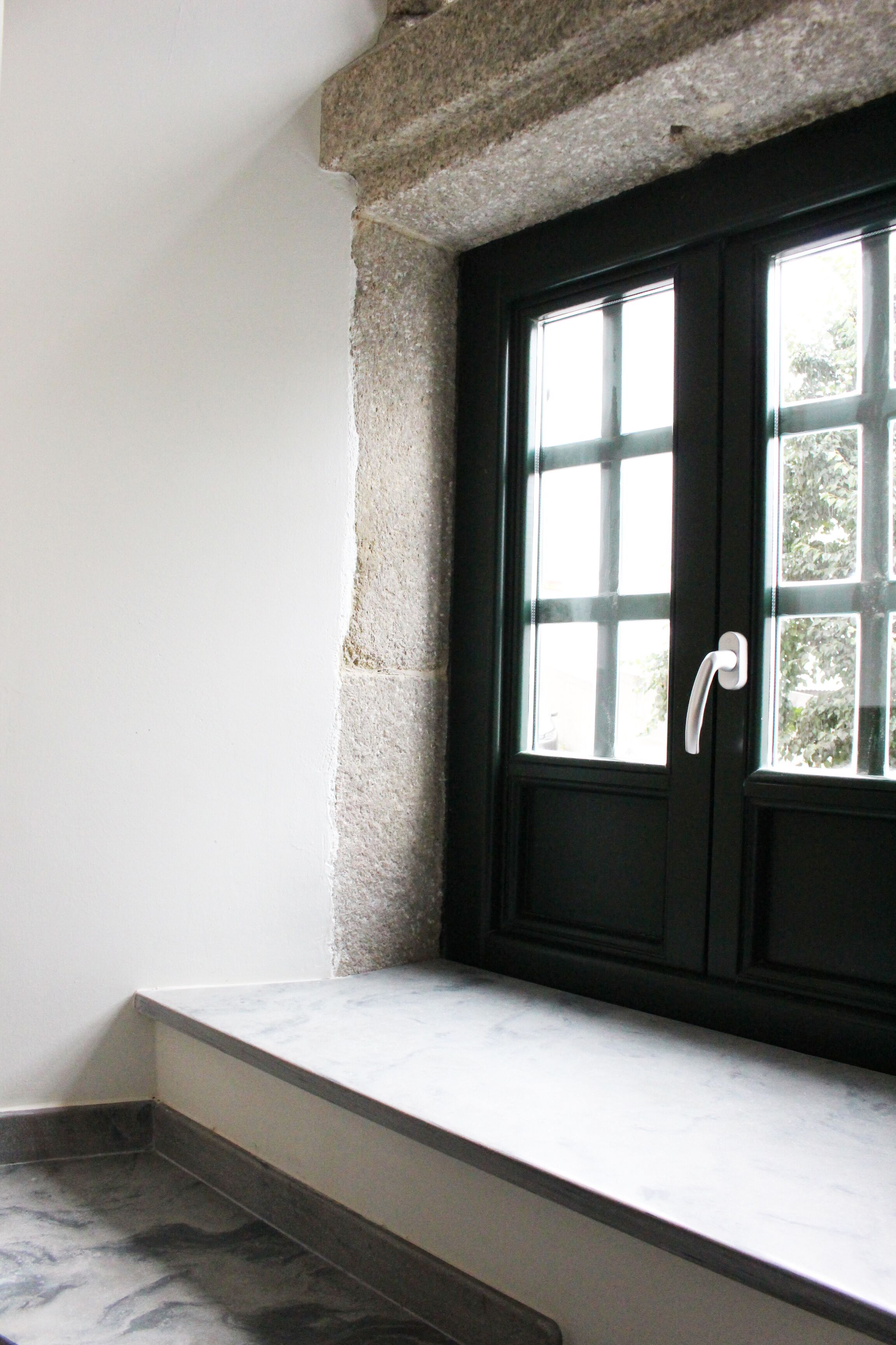 Una puerta negra con manija blanca, una ventana con múltiples vidrios y un alero de piedra.