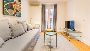 Una sala de estar moderna con un sofá gris, una mesa de centro de vidrio, un televisor de pantalla plana y un cuadro de una mujer en un bote.