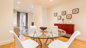 Un comedor moderno con una mesa de vidrio rodeada de sillas blancas, un armario rojo con cuadros enmarcados y vistas a un salón con sofá y una mesa.