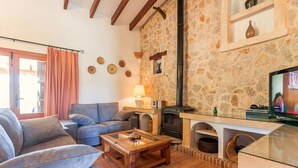 A cozy living room with a stone wall, a fireplace, a television, and a sofa. - Villa Tatoli is a spacious and traditional 4 bedroom villa with private pool (Pollensa)