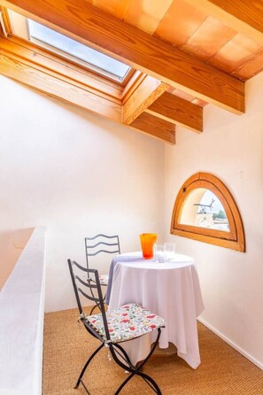 Un pequeño comedor con una mesa, sillas, una ventana de arco y techo de madera.