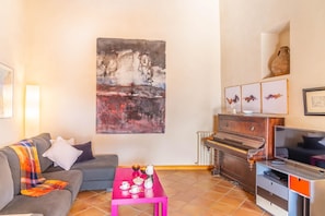Uma sala de estar com sofá, mesa de centro, piano e televisão.