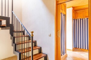 A staircase with wooden steps and black railings, leading to a room with striped curtains and wooden cabinets.