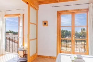 Una habitación con cama, una mesita y vistas a un balcón con barandilla.