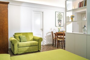 A room with a green sofa, a dining table with chairs, a white door, and a bookshelf with books and decorative items. - L 'Antica Pigna Chateau - Olive Tree Apartment (Vico Equense)