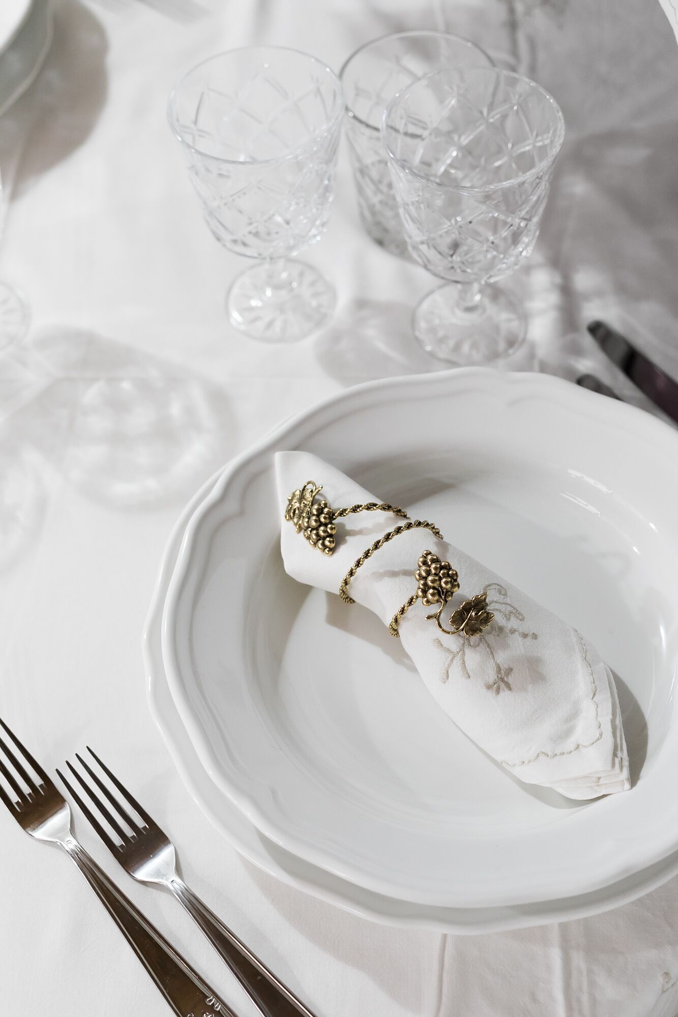 A white table setting with a plate holding a napkin wrapped in a decorative cloth, accompanied by a fork and a knife.