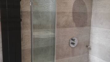 A glass-enclosed shower stall with a handheld showerhead, a wall-mounted towel rack, and a floor drain.